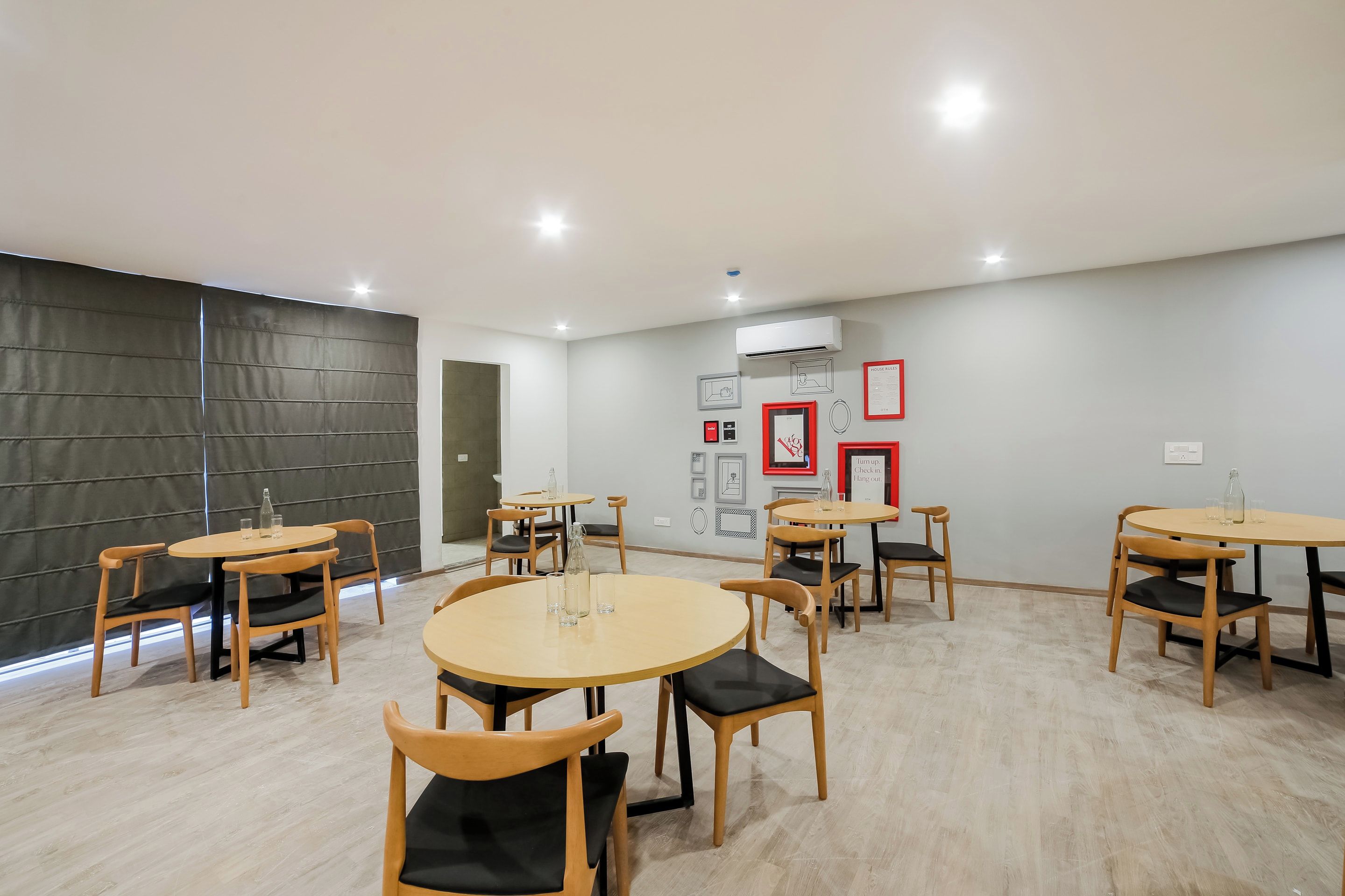 Een moderne vergaderruimte met ronde tafels en stoelen, een airconditioningapparaat en kunstwerken in lijsten aan de muren.