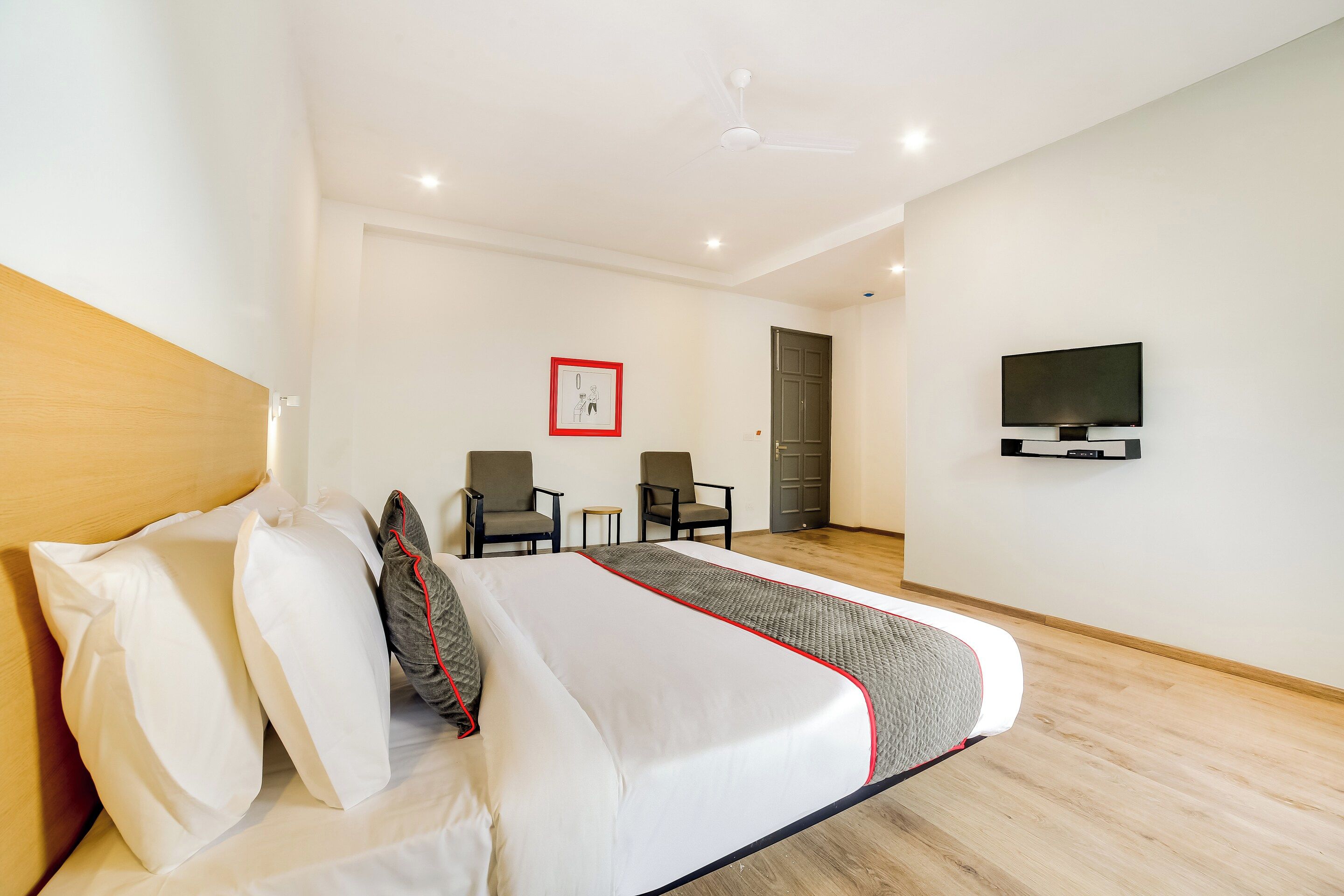 Een hotelkamer met een bed, twee stoelen, een televisie en een deur.