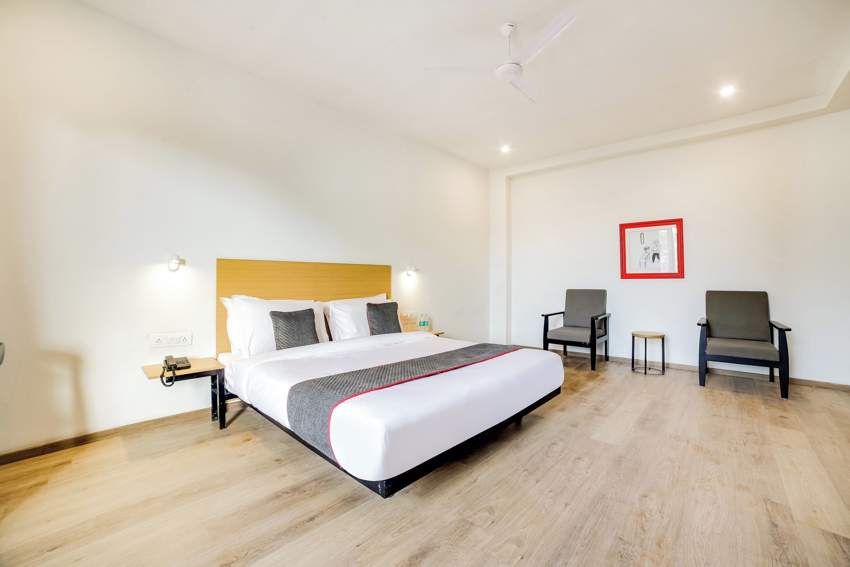 Een hotelkamer met een bed, nachtkastjes, een bureau, twee stoelen, een klein krukje en een plafondventilator.