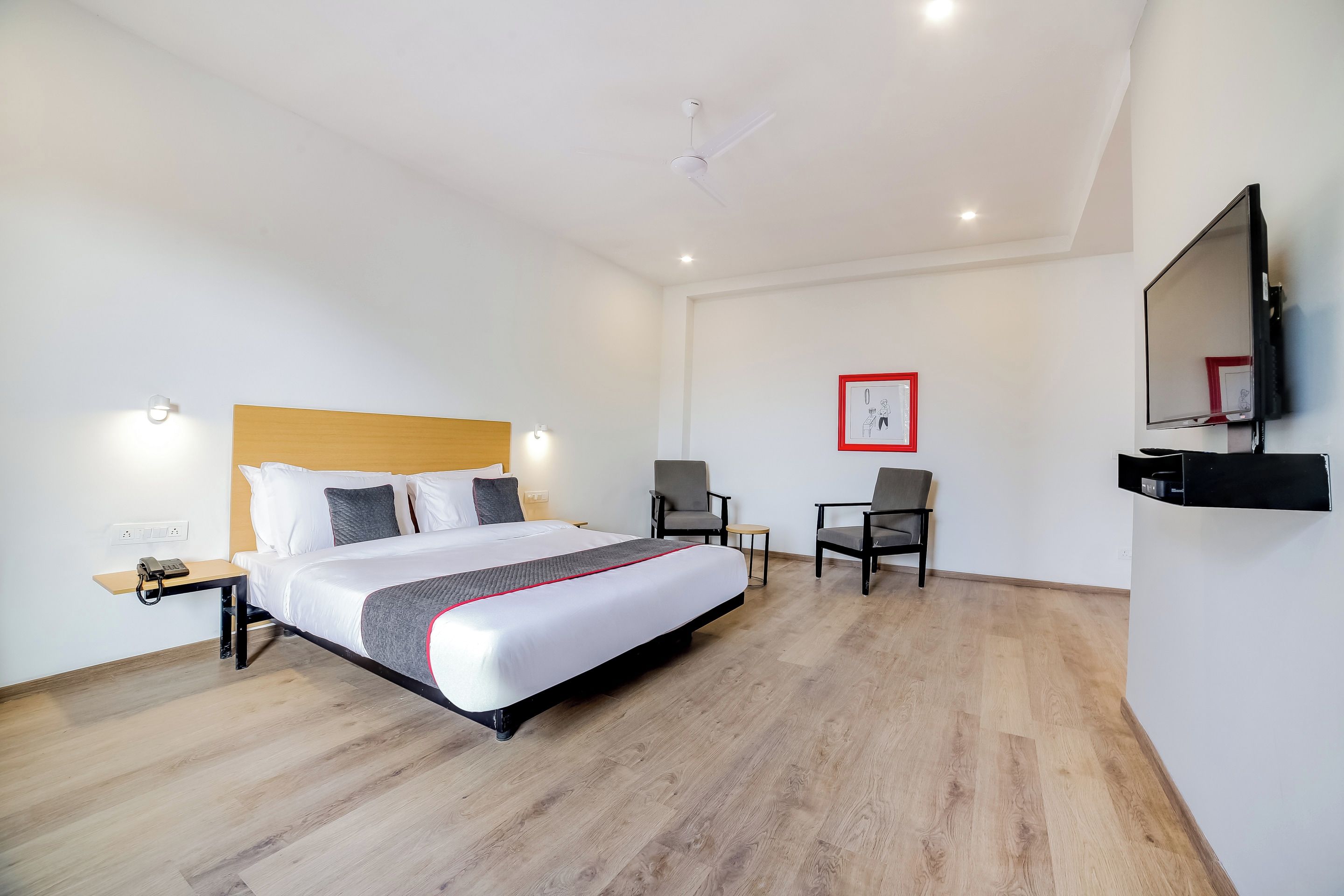 A hotel room with a bed, bedside table, chair, TV, and a small table with a phone.