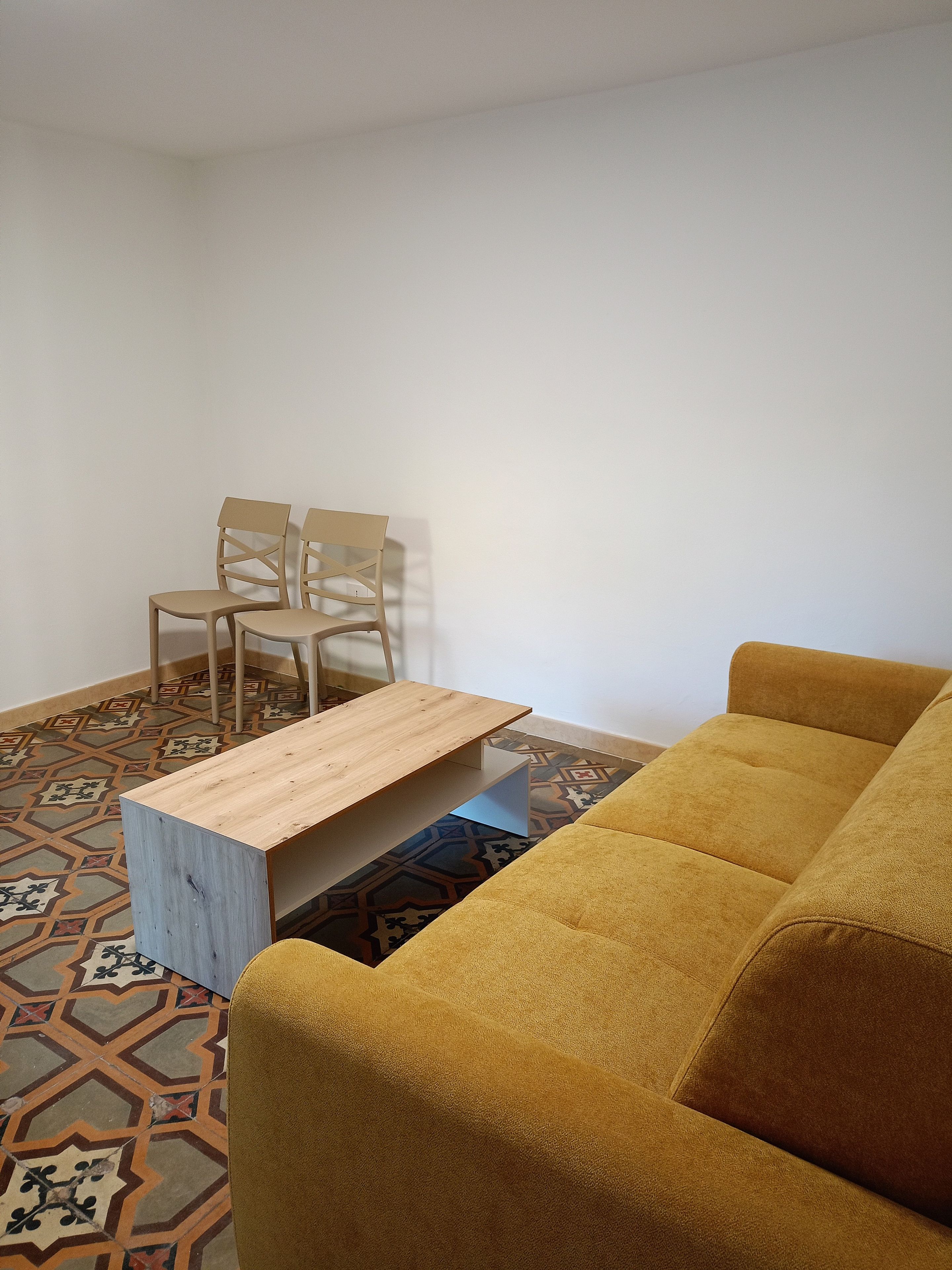 Une pièce avec un canapé jaune, une table basse en bois et un sol à motifs.