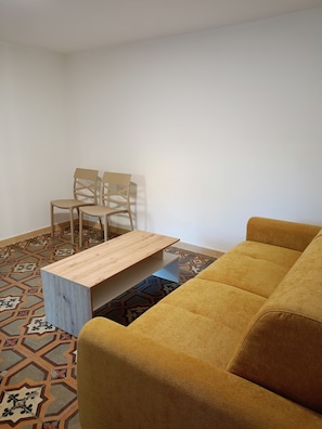 A room with a yellow sofa, a wooden coffee table, and a patterned floor.