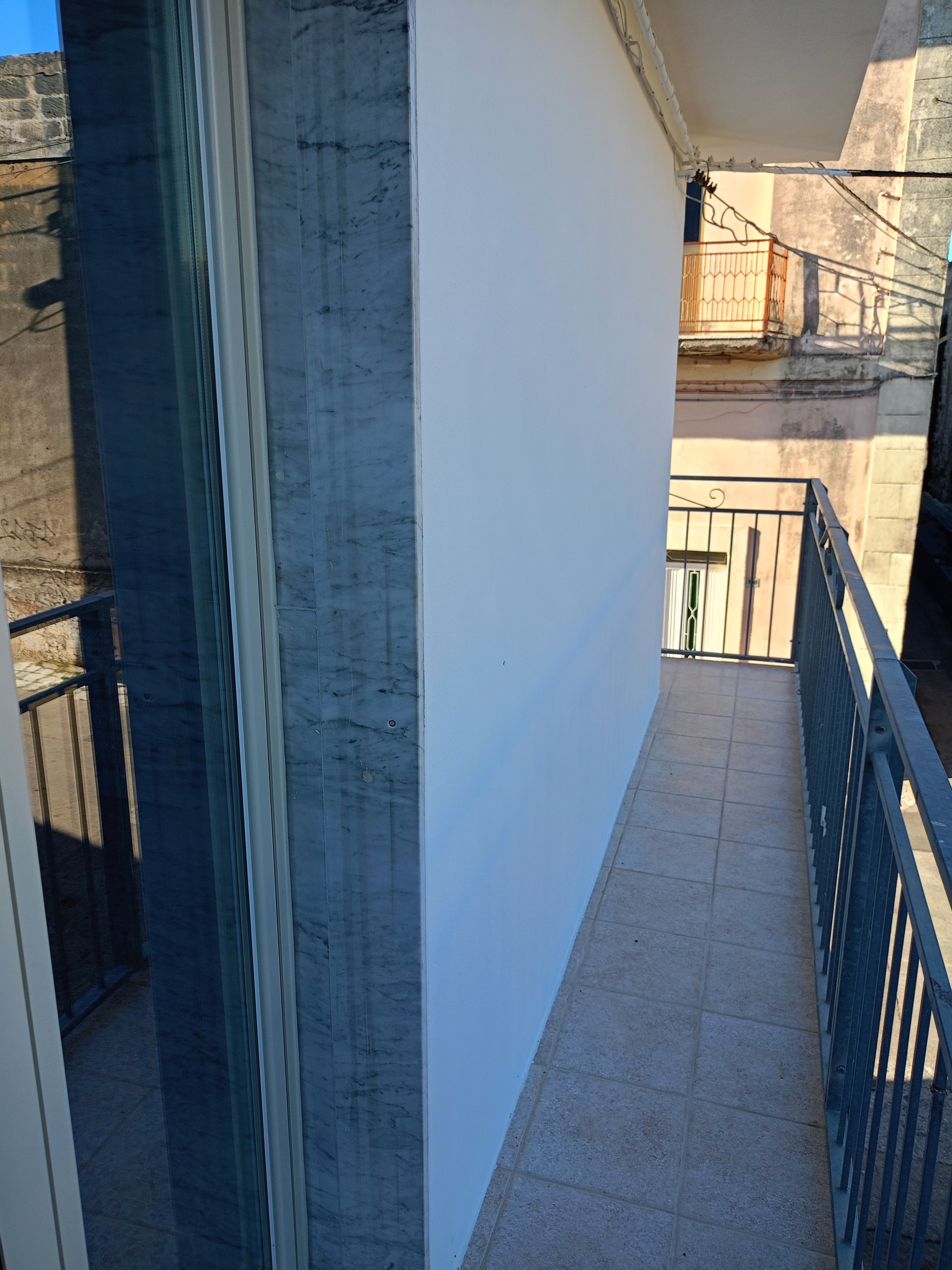 A narrow corridor with a tiled floor, a white wall, and a metal railing.