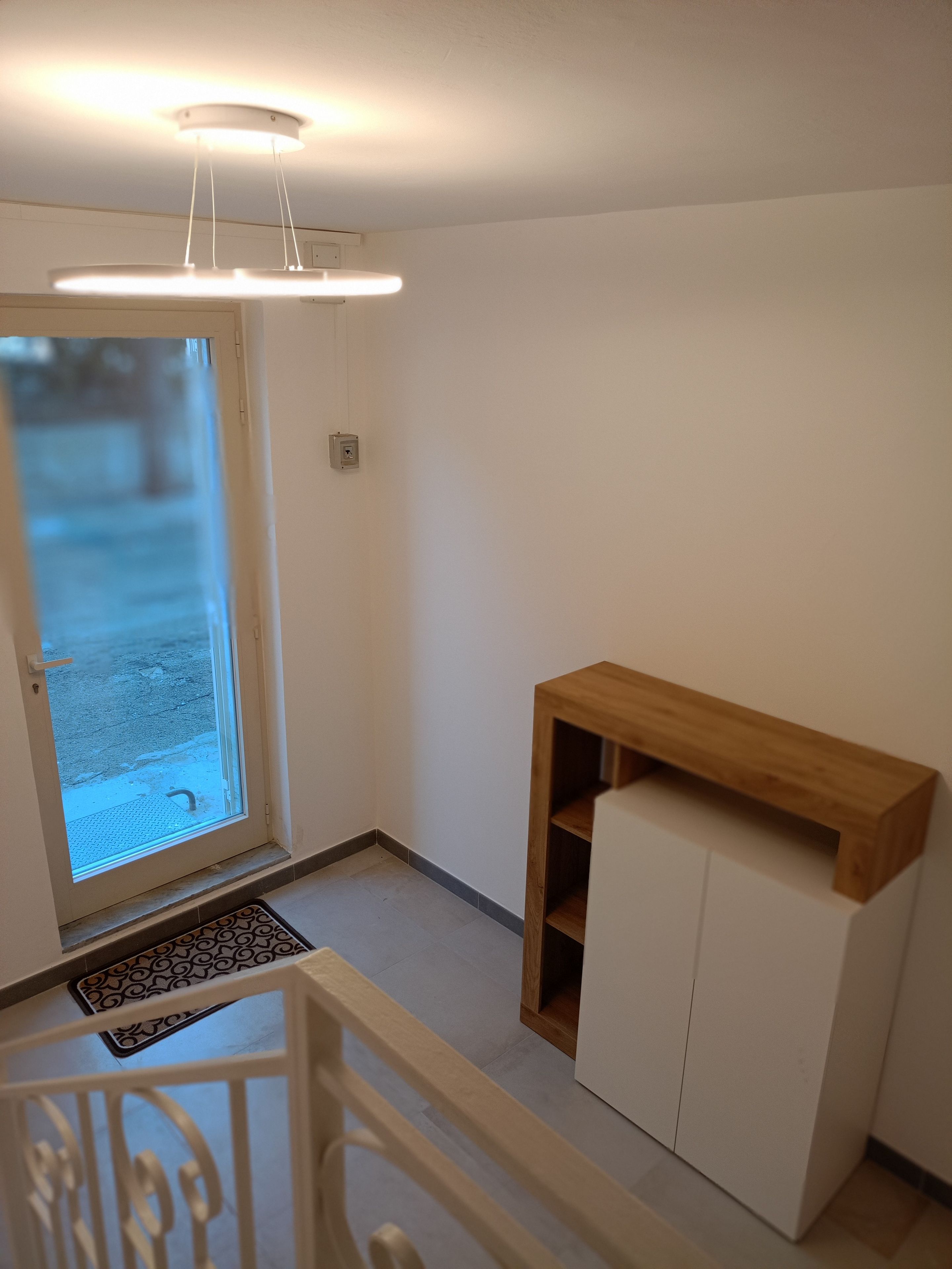 A room with a door leading to an outdoor area, a small wooden shelf, and a white cabinet.