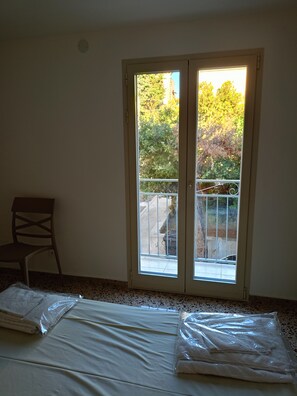 Quarto com uma grande porta de vidro deslizante que dá para uma varanda, uma cadeira e uma cama com cobertura branca.