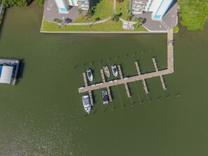 Eine Vogelperspektive auf einen Yachthafen mit angestaubten Booten, einer anlegenden Mole und Gebäuden im Hintergrund.