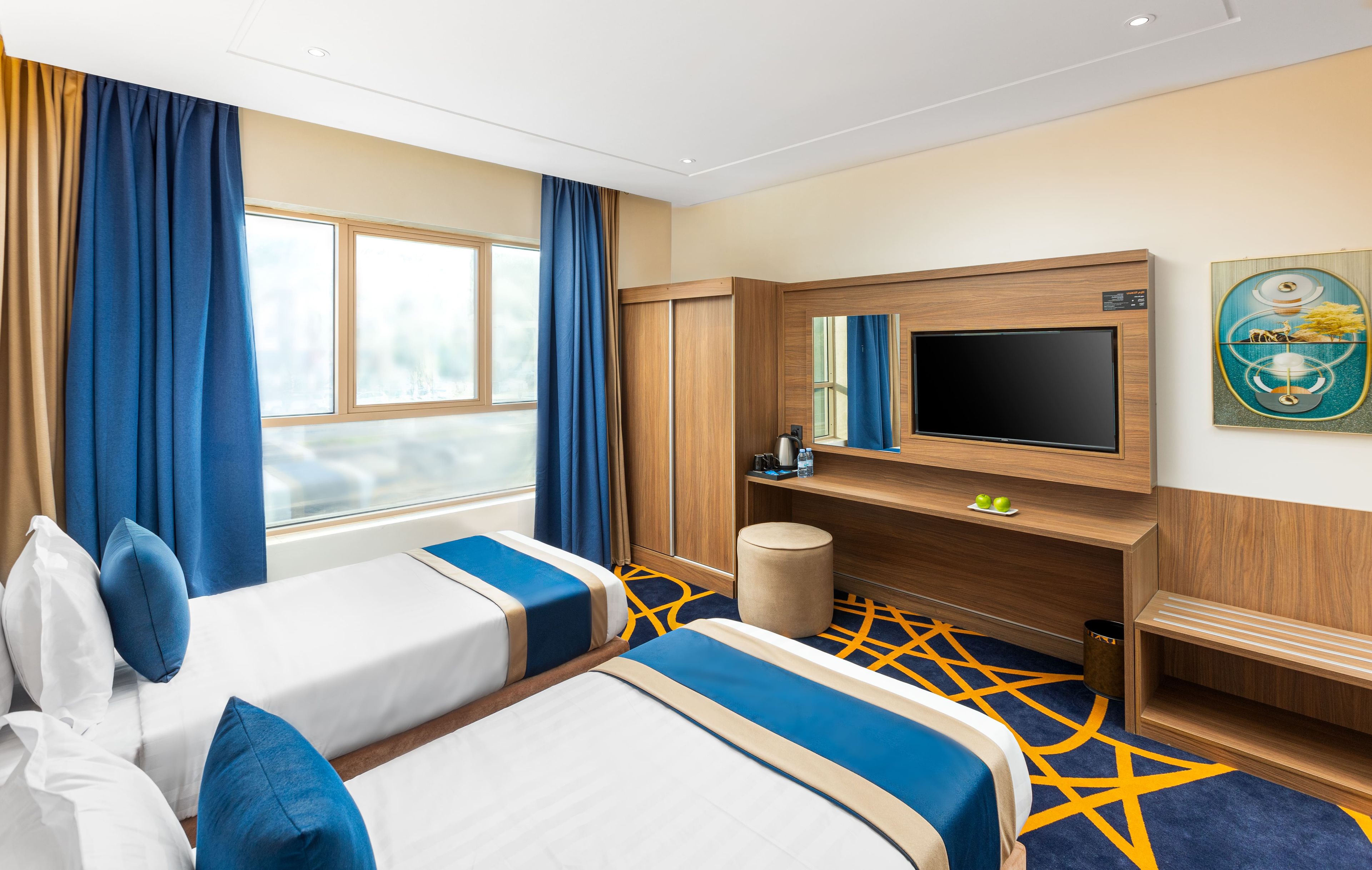 A hotel room with two beds, a TV, a desk, and a window with curtains.