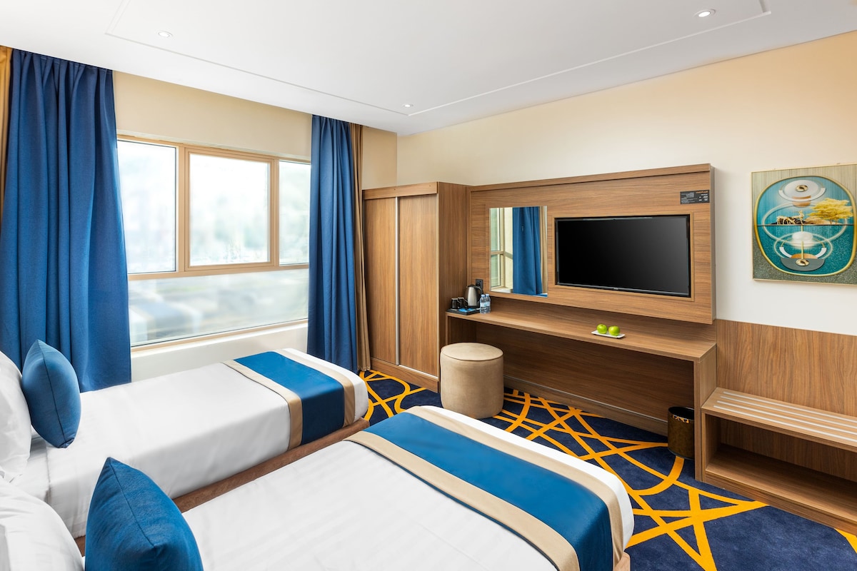 Een hotelkamer met twee bedden, een televisie, een bureau en een raam met gordijnen.