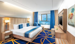 Hotelkamer met een groot bed, een televisie, een bureau en een raam met uitzicht op een gebouw en bomen.
