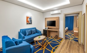 Habitación de hotel moderna con sofá azul, una mesita redonda, televisor de pantalla plana y alfombra estampada.