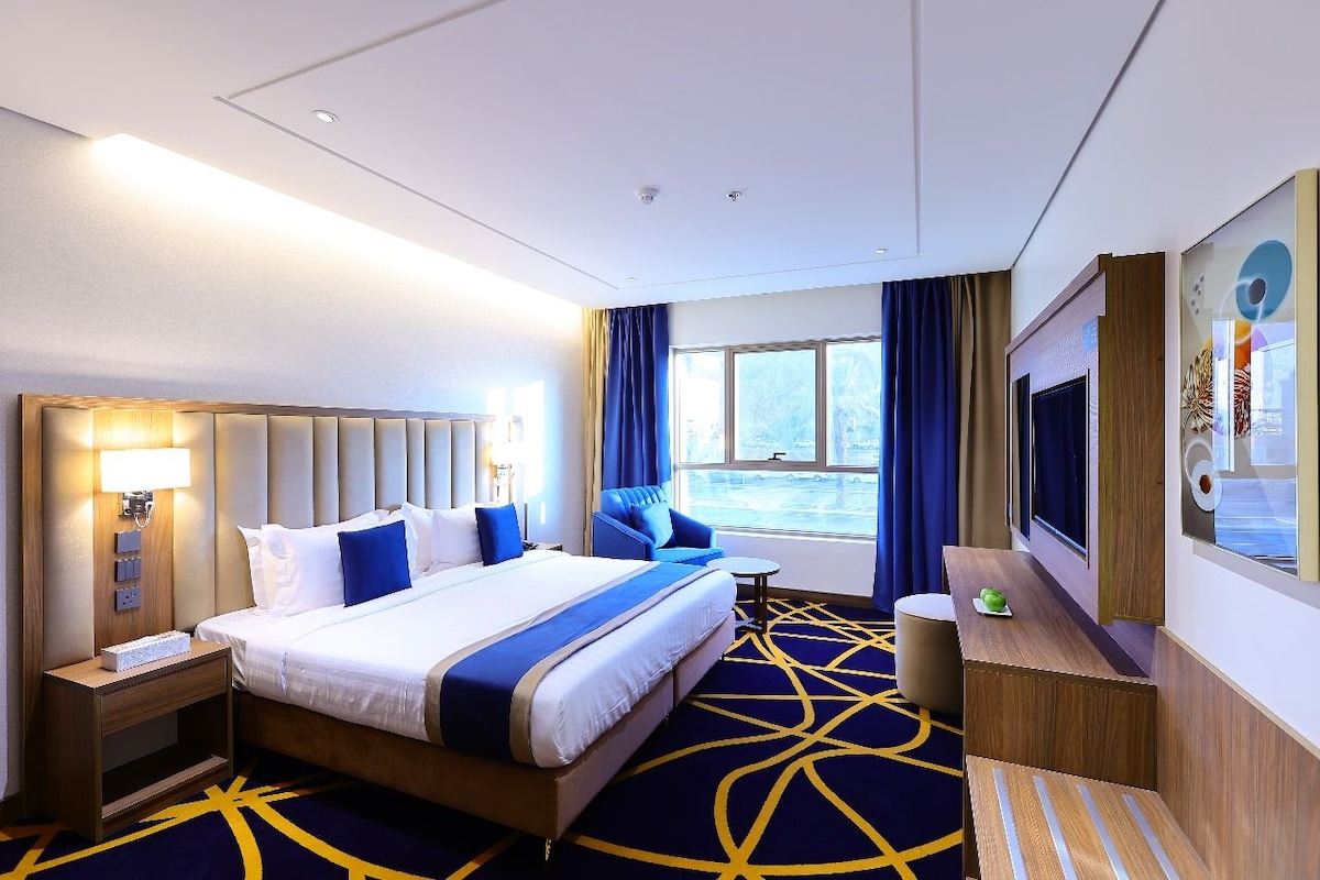 Een hotelkamer met een groot bed, een televisie, een bureau en een raam met gordijnen.