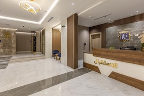 Een hotel receptie met een marmeren vloer, een receptiebalie en een houten paneelwand.