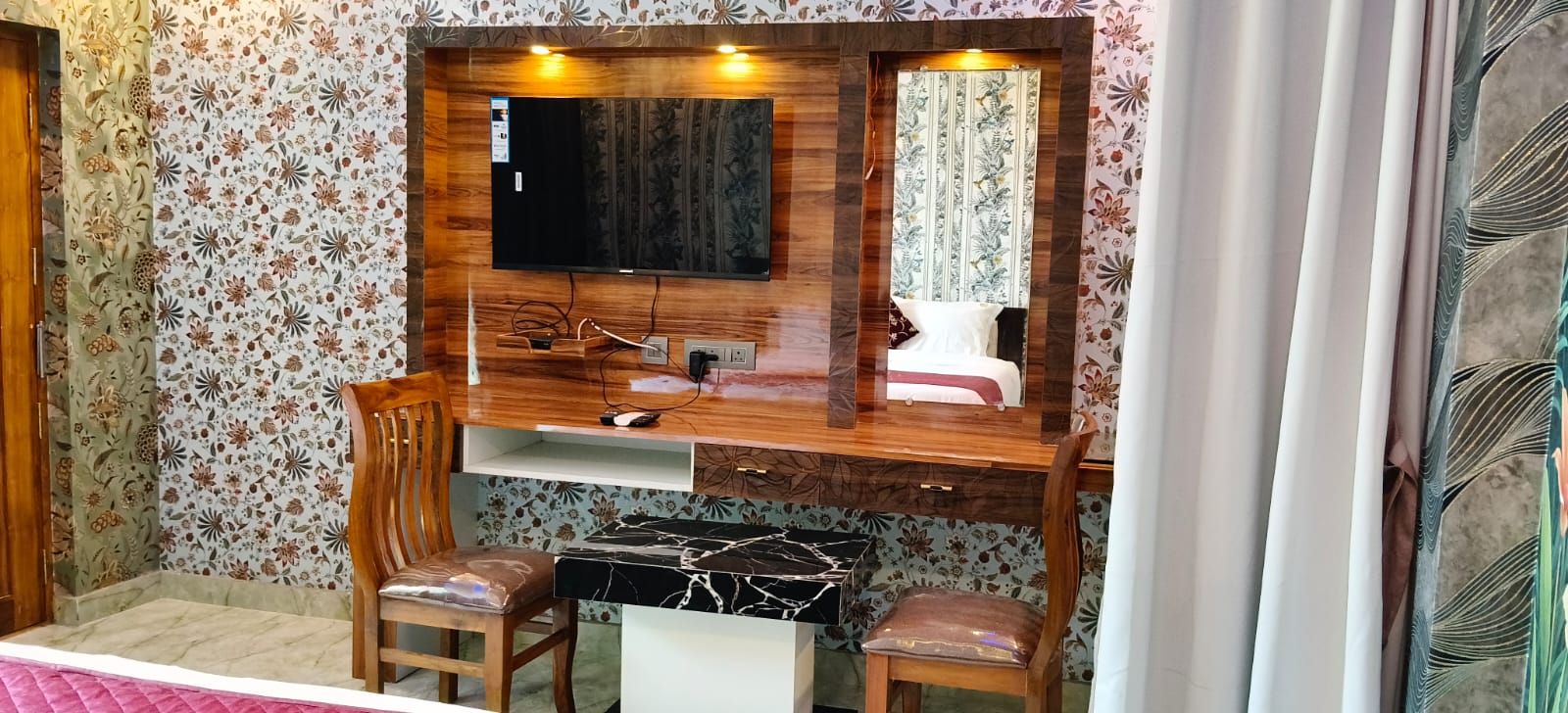 Un dormitorio con un escritorio de madera, un televisor y una cama con papel tapiz floral.