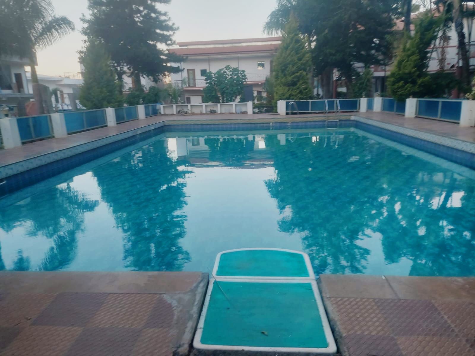 A swimming pool with a clear blue water surface, surrounded by a low wall and trees.