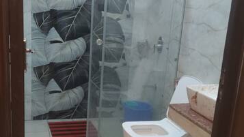 A bathroom with a glass shower enclosure, a toilet, and a sink with a marble countertop.