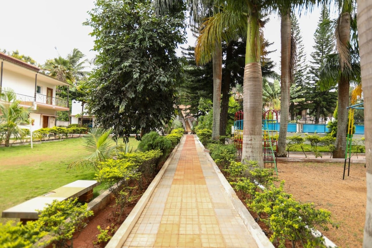 A pathway lined with greenery and palm trees, leading to a building with a balcony.