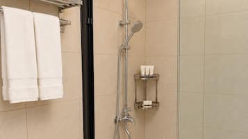 Une salle de bain moderne avec une douche à parois de verre, des toilettes sur lesquelles est posée une serviette, et une étagère contenant des articles de toilette.