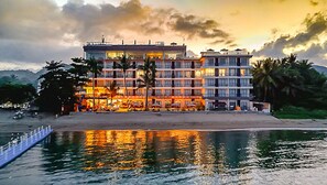Ein mehrstöckiges Hotel mit Pool im Vordergrund, das Gebäude und den Himmel darin spiegelt.