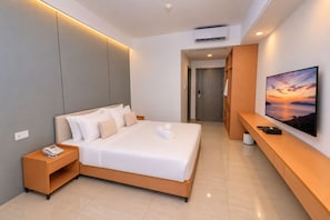A modern hotel room with a large bed, a bedside table with a phone, a flat-screen TV, and a wooden bench.
