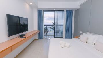 Une chambre d’hôtel avec un lit, un téléviseur posé sur une console en bois, un balcon avec vue et une grande fenêtre avec des rideaux.