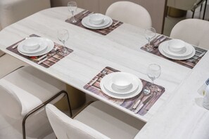 A dining table set with white plates, cutlery, and glasses, with chairs around it. - StayShort - Elegant 1 Bedroom in JVC that Sleeps 2 (JVC)