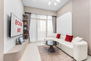 A modern living room with a sofa, a coffee table, a TV, and a bookshelf. - StayShort - Elegant 1 Bedroom in JVC that Sleeps 2 (JVC)
