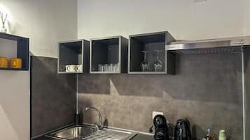 A modern kitchen with a stainless steel sink, black cabinets, and a coffee machine.