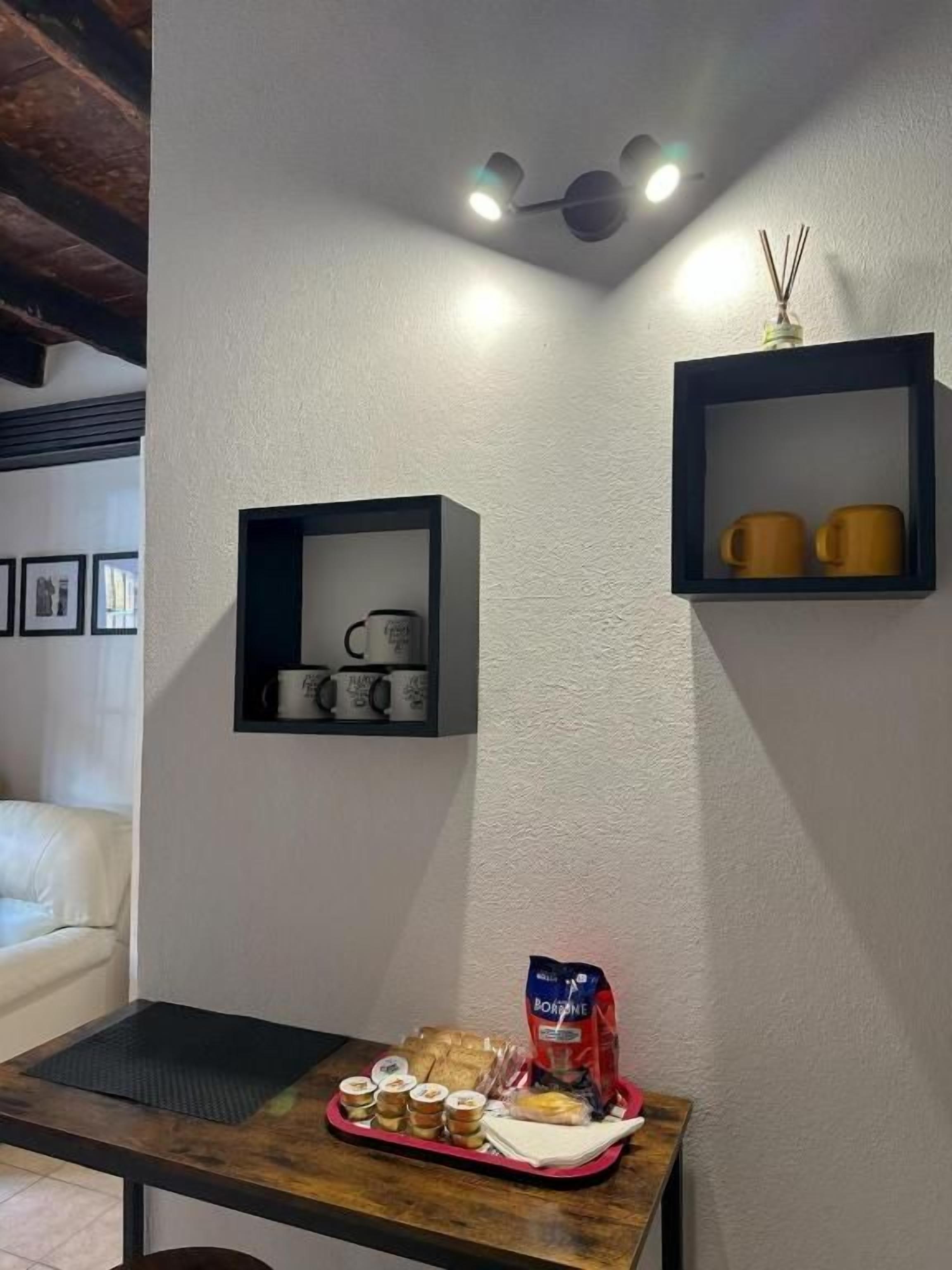 Una habitación con una mesa de madera, una bandeja con alimentos, una estantería con tazas y un estante de pared con adornos.