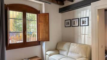 A room with a wooden bench, a white sofa, and a window with a wooden shutter.