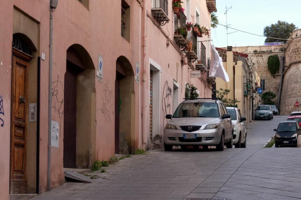 Una calle estrecha con coches aparcados y edificios con balcones.