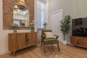 A living room with a brick wall, a green armchair, a wooden cabinet, a mirror, a potted plant, and a television. - San Francesco Boutique House by Wonderful Italy. (Torino)