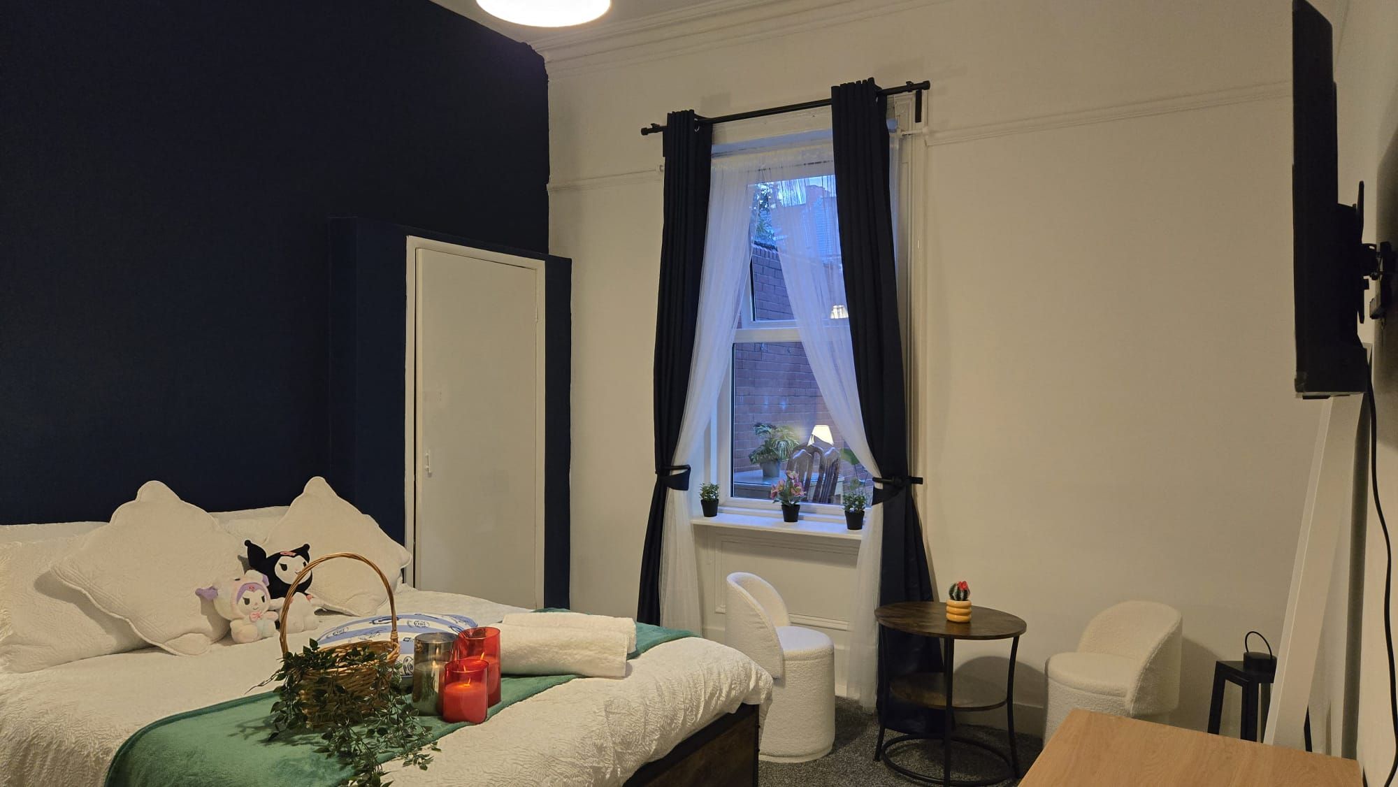 Une chambre à coucher avec un lit, une fenêtre avec des rideaux, une petite table et une chaise.