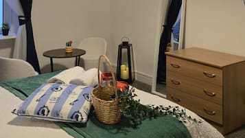 A hotel room with a bed, a television mounted on the wall, a dresser, a small table with a lamp, and a window with curtains.