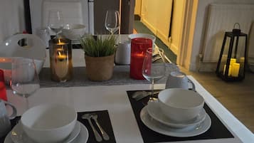 A dining table set with plates, cutlery, and glasses, with a potted plant and candles on the table.
