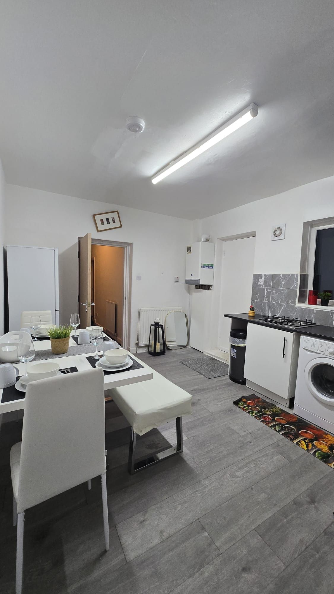Une cuisine moderne avec un coin repas, des meubles blancs, un four encastré et un lave-linge.