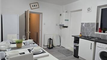 Une cuisine moderne avec un coin repas, des meubles blancs, un four encastré et un lave-linge.