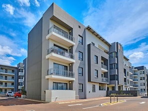 A multi-story residential building with balconies, a parking area, and a clear sky. - Regentis Executive Stays at The Atrium Unit 164 (Johannesburg)
