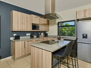 A modern kitchen with wooden cabinets, a built-in microwave, a stainless steel refrigerator, and a window with a view of greenery. - Regentis Executive Stays at The Atrium Unit 151 (Johannesburg)