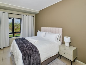 A bedroom with a bed, a nightstand, a window with curtains, and a view outside. - Regentis Executive Stays at The Atrium Unit 154 (Johannesburg)
