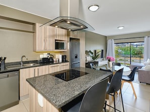 A modern kitchen with a central island, built-in appliances, and a dining area with a view. - Regentis Executive Stays at The Atrium Unit 154 (Johannesburg)