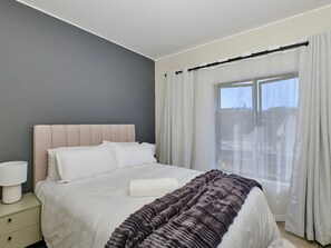 A bedroom with a bed, a bedside table, and a window with curtains. - Regentis Executive Stays at The Atrium Unit 163 (Johannesburg)