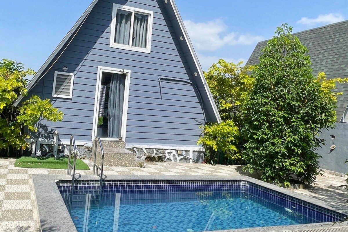 Una propiedad residencial con piscina, techo triangular y césped bien cuidado.