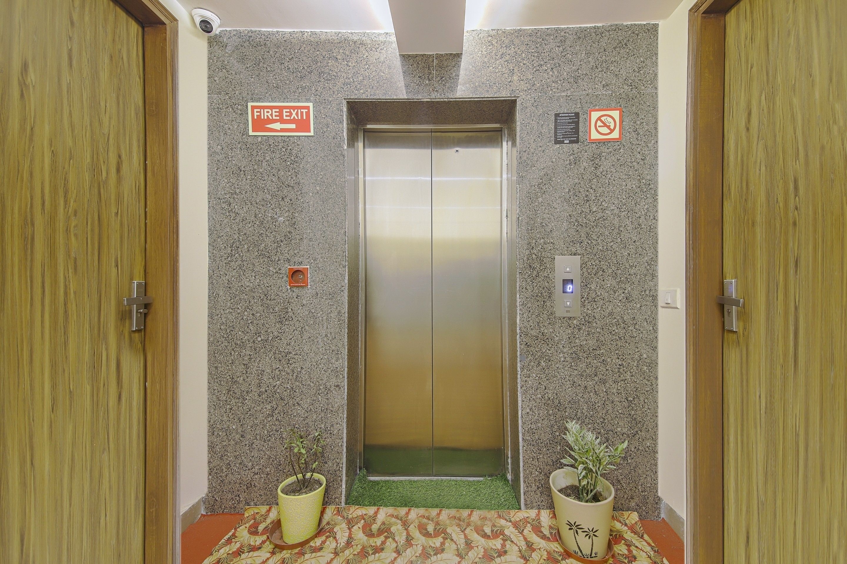 Een lift met een bord voor branddeur, een rookverbodsge teken en twee potplanten aan weerszijden.
