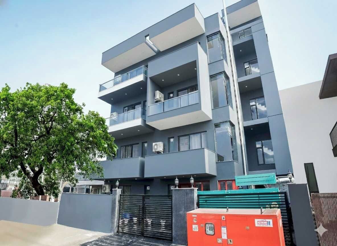 A multi-story building with balconies, a gated entrance, and a tree in the foreground.