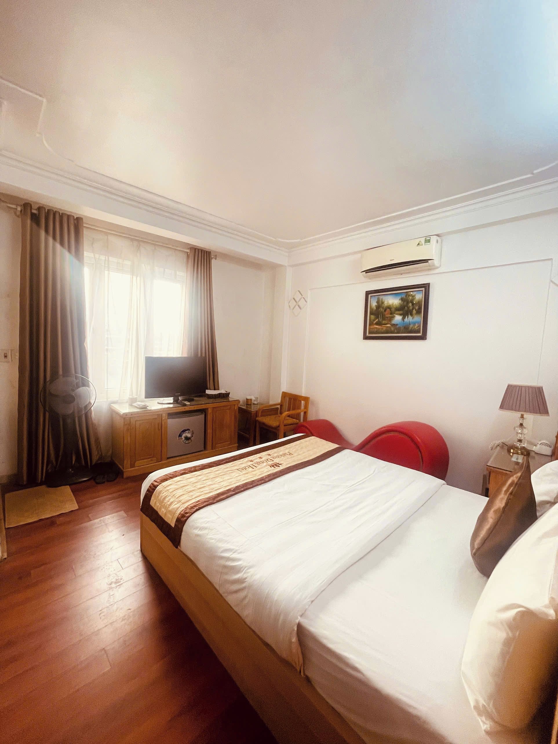 Une chambre d’hôtel avec un lit, un bureau équipé d’un ordinateur, une chaise, un téléviseur et une fenêtre avec des rideaux.