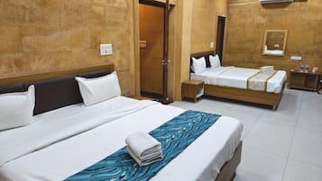 Habitación de hotel con dos camas, cabecera de madera, corredor de cama azul con estampado y una mesita de noche con lámpara.