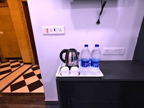 Ein Hotelzimmer mit einem Schachbrettmuster-Boden, einem schwarzen Schrank, einer Ablage mit einem Wasserkocher, zwei Tassen und zwei Wasserflaschen.