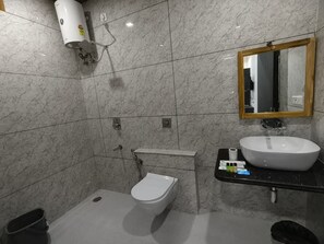 A bathroom with a toilet, sink, mirror, and towel dispenser.