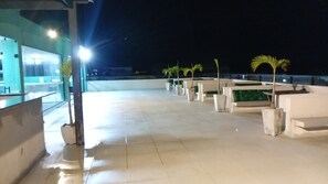 Una terraza en la azotea con plantas en macetas, zona de estar y vistas al cielo nocturno.