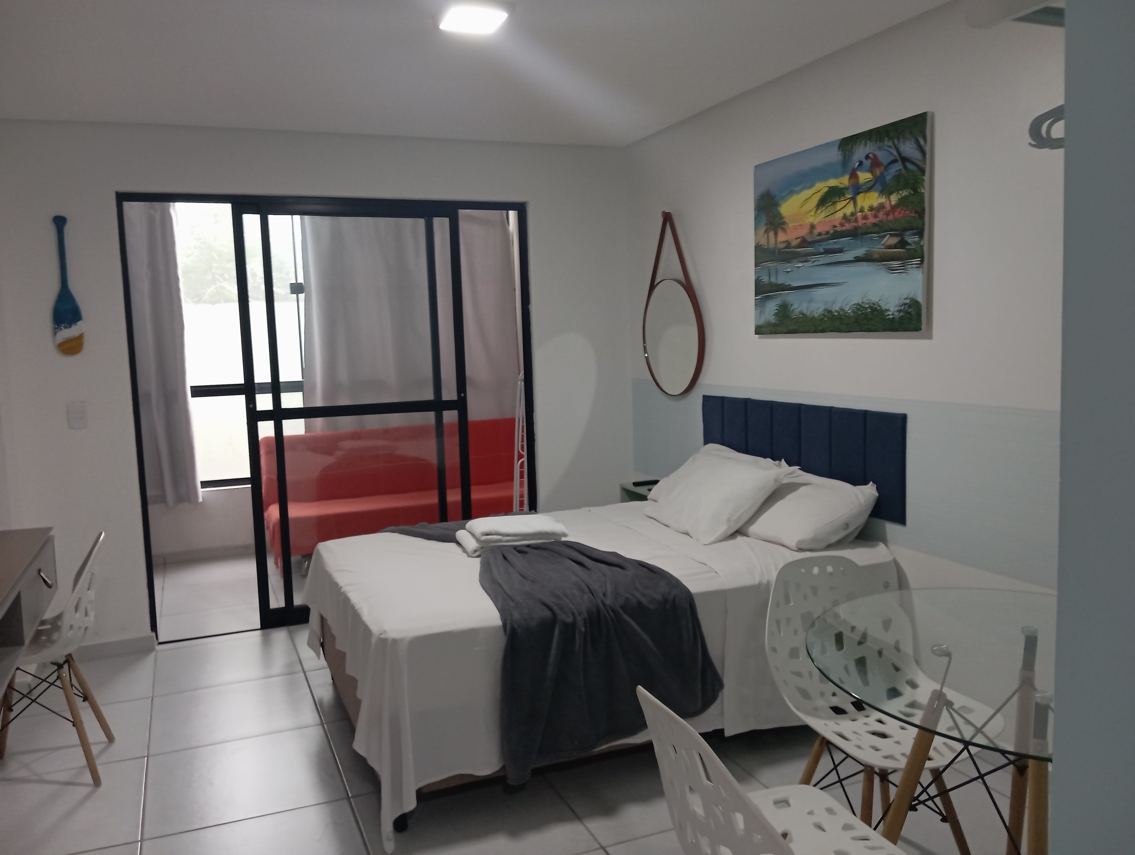 A bedroom with a bed, a chair, a window with curtains, and a painting on the wall.